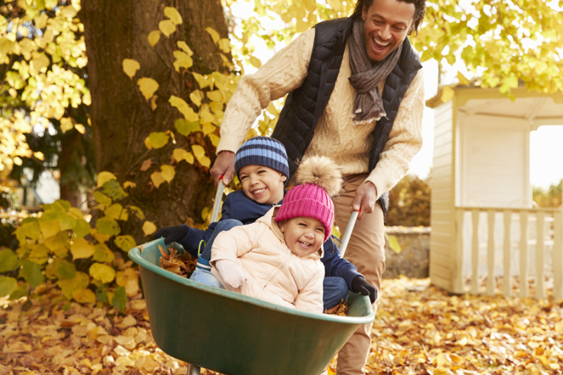 Father In Autumn Garden Gives Children Ride.