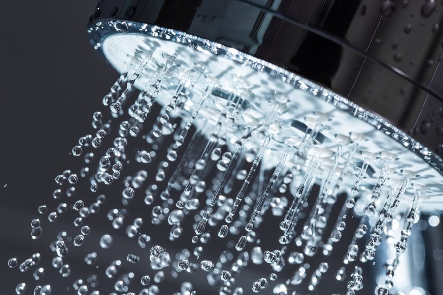 Close-up of water flowing steadily from a showerhead against a black background.
